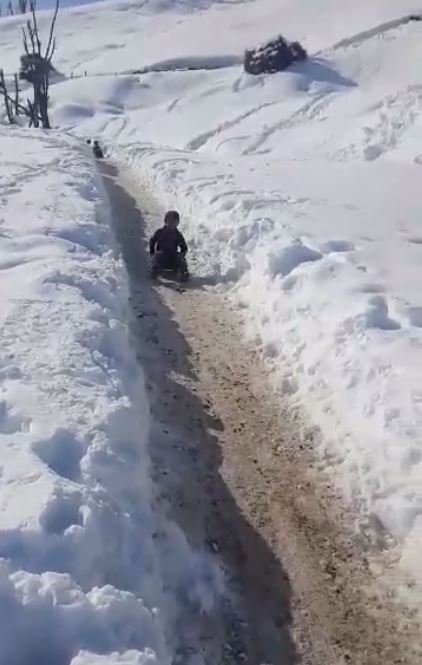 Köylü çocuklar, karla kaplı köy yolunu kayak yoluna çevirdi
